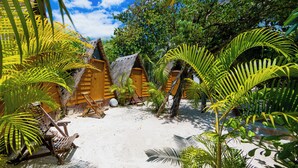 Een tropisch resort met rieten hutten, palmbomen en een zandstrand.