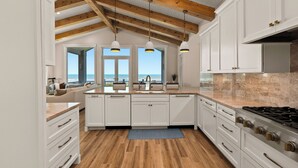 Una cucina moderna con mobili bianchi, soffitto in legno e vista all'esterno.