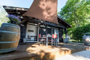 A wooden deck with a covered seating area, large barrels, and a rustic building with a large awning. - Elite - LACQUY - Gîte (LACQUY)