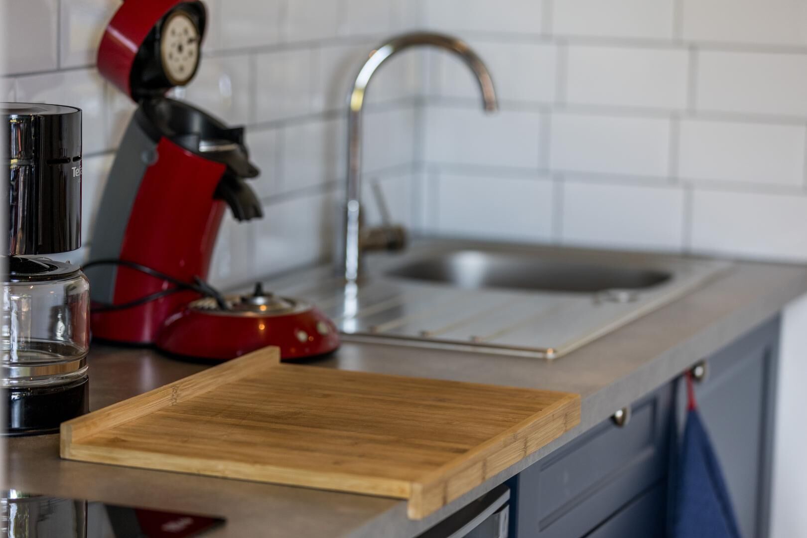 A kitchen counter with a coffee maker, a red kettle, and a wooden cutting board.