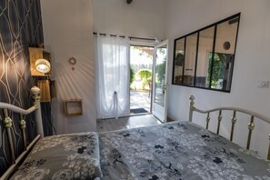 A bedroom with a bed, a bedside lamp, a small wooden shelf, a mirror, and a door leading to an outdoor area. - Elite - LACQUY - Gîte (LACQUY)