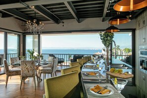 Een eetgedeelte met uitzicht op zee, met een lange tafel gedekt voor een maaltijd, stoelen en een kroonluchter.