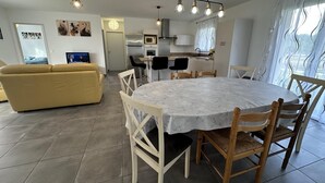 Ein modernes Wohnzimmer mit einem gelben Sofa, einem Esstisch mit weißen Stühlen und einer Küchenzeile inklusive Kühlschrank, Mikrowelle und Herd.