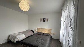 Ein Schlafzimmer mit zwei Betten, einem Holz-Kopfteil, einer Wandleuchte und einem dekorativen Vorhang.