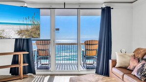 A modern living room with a large sliding glass door to a balcony overlooking a beach. - 1002 Oceanfront Pelican Beach Resort Amazing Location Multiple Pools & Hot Tubs (Destin)