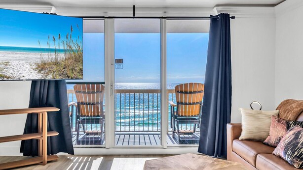 A modern living room with a large sliding glass door to a balcony overlooking a beach.