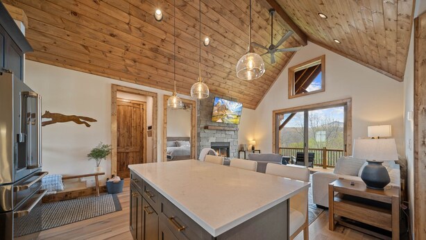 A spacious kitchen with a large island, wooden ceiling, and pendant lighting.
