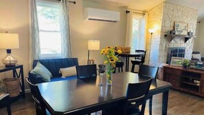 A dining area with a dark wooden table, black chairs, and a vase of sunflowers. There is a blue sofa, a lamp, and a wall-mounted air conditioner.