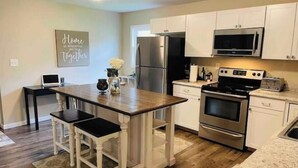 A modern kitchen with white cabinets, a wooden island, stainless steel appliances, and a laptop on the counter.