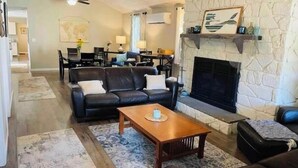 A living room with a fireplace, a sofa, a coffee table, and a dining area in the background.