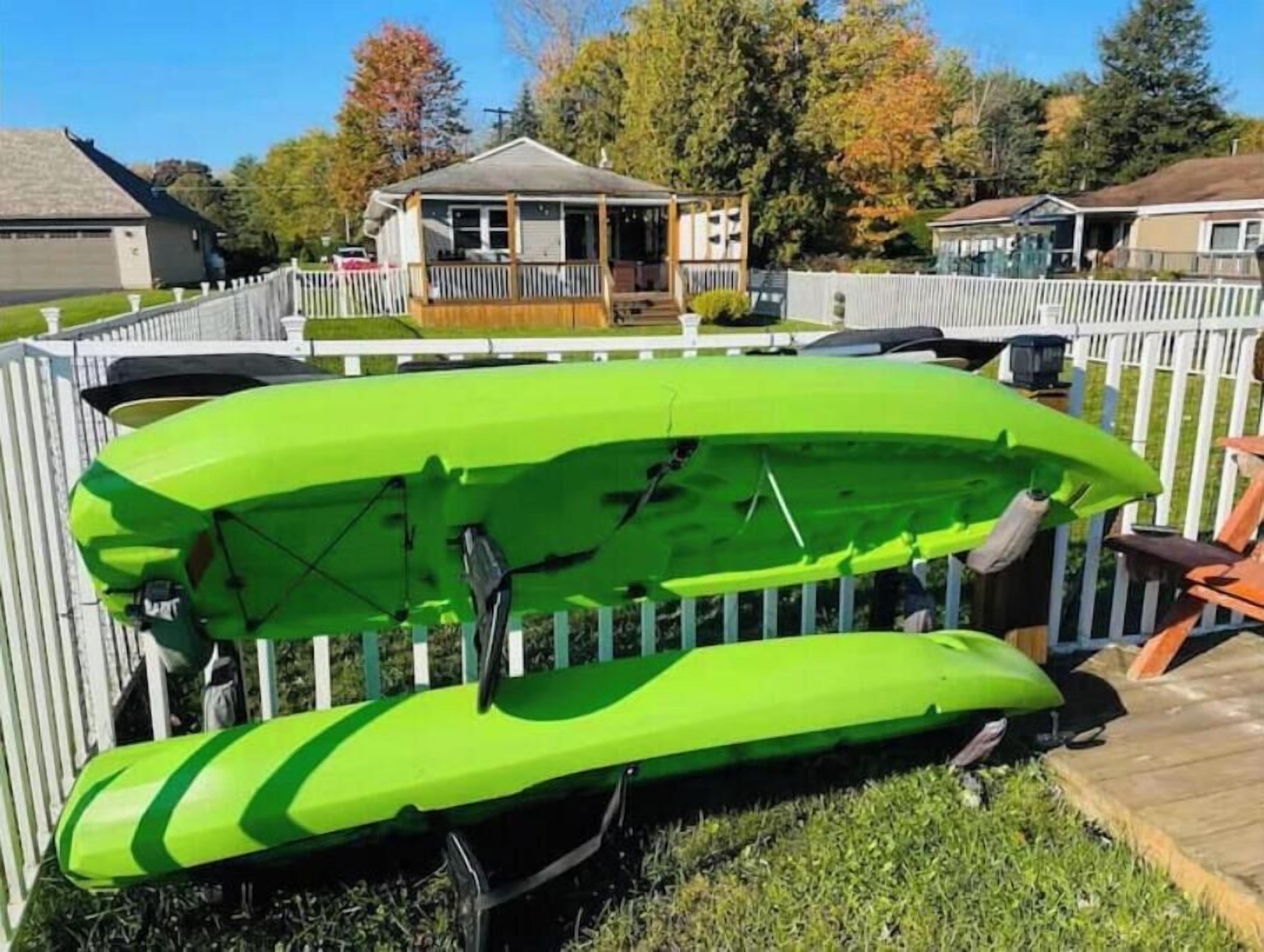 A green kayak stored in a fenced backyard with a house in the background.