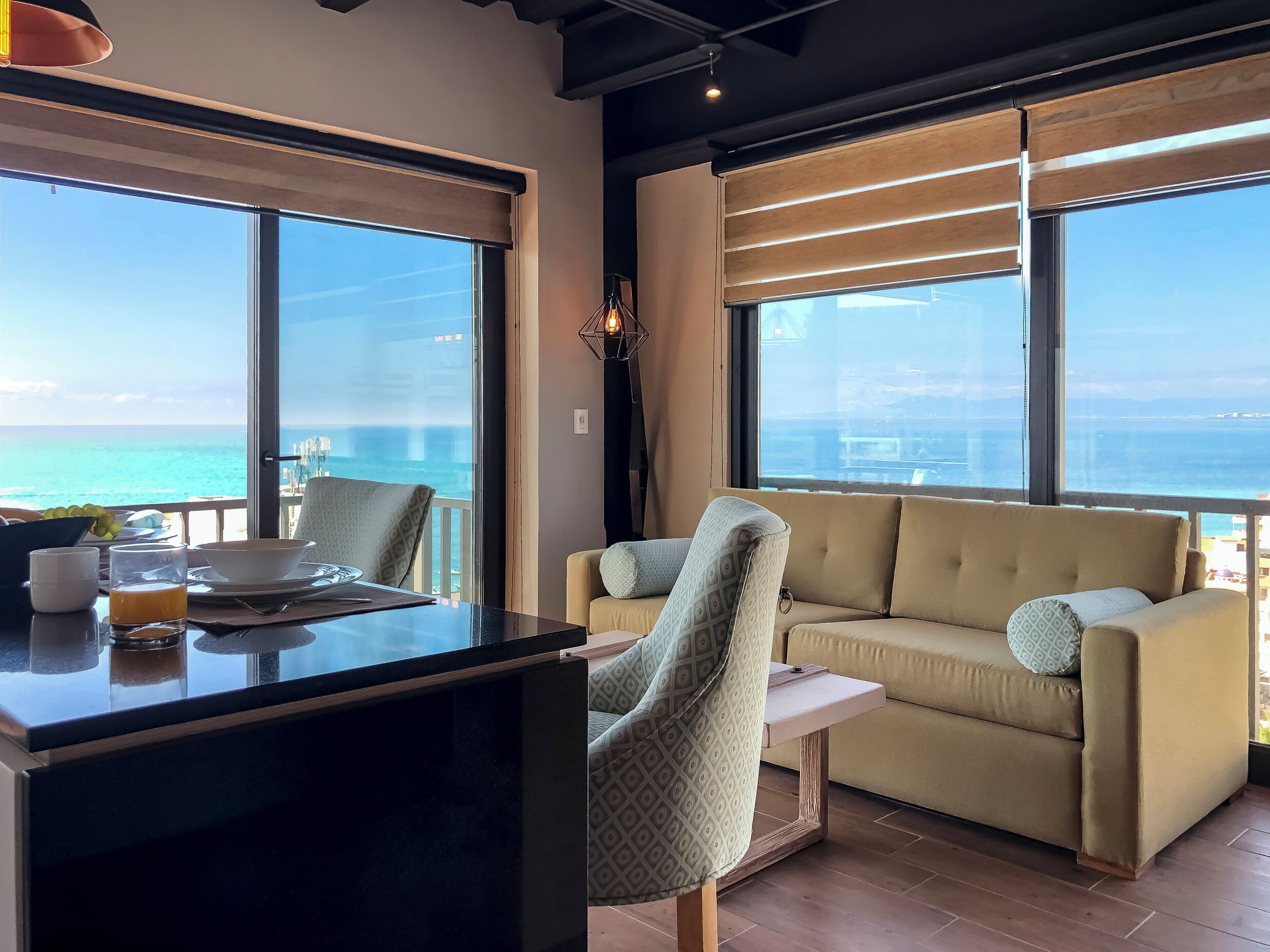 Een moderne kamer met een groot raam met uitzicht op de zee, een bank, een stoel en een kleine tafel met ontbijtartikelen.