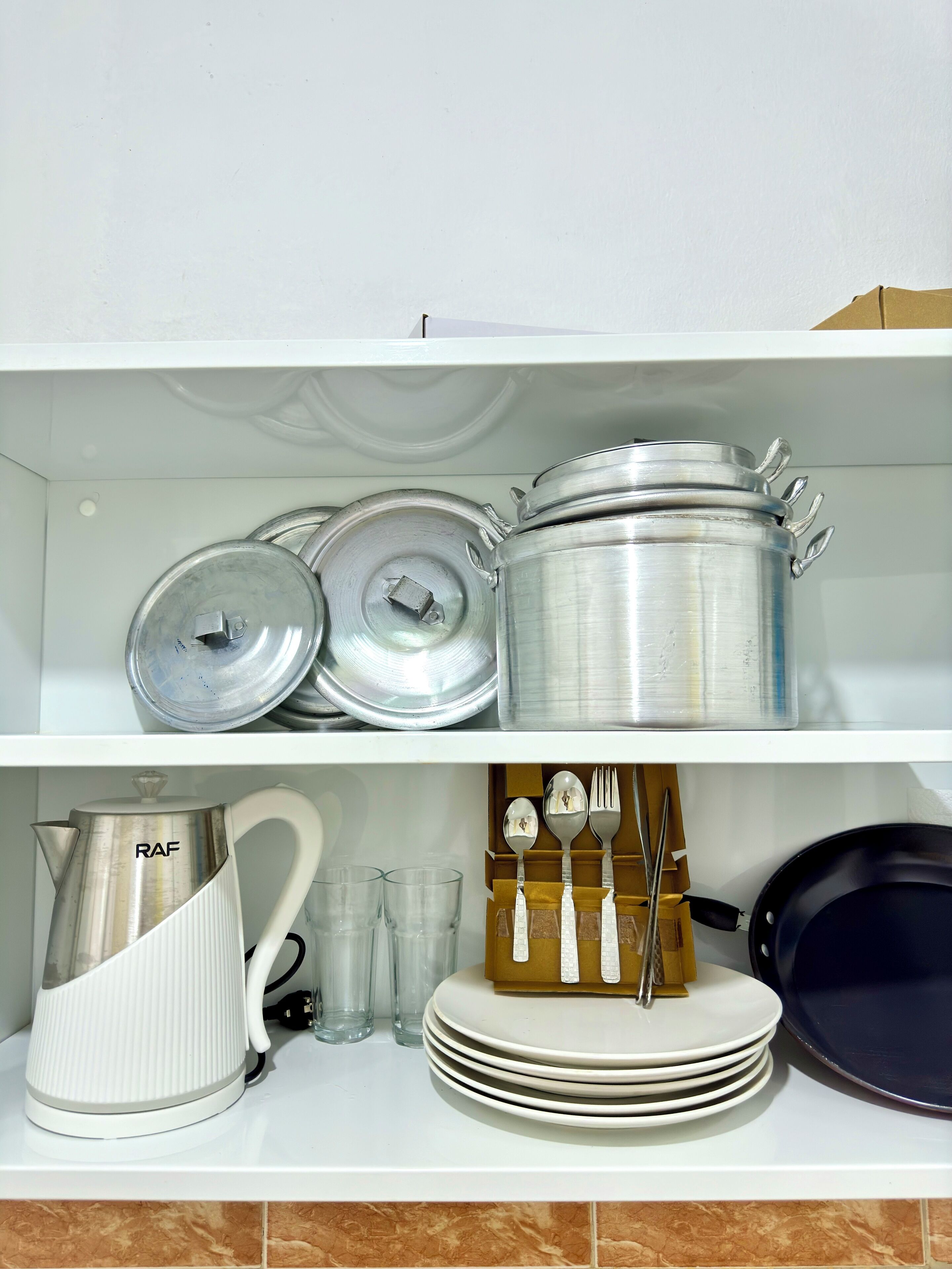 Una repisa de cocina con diversos utensilios, incluyendo ollas, sartenes, una tetera y cristalería.