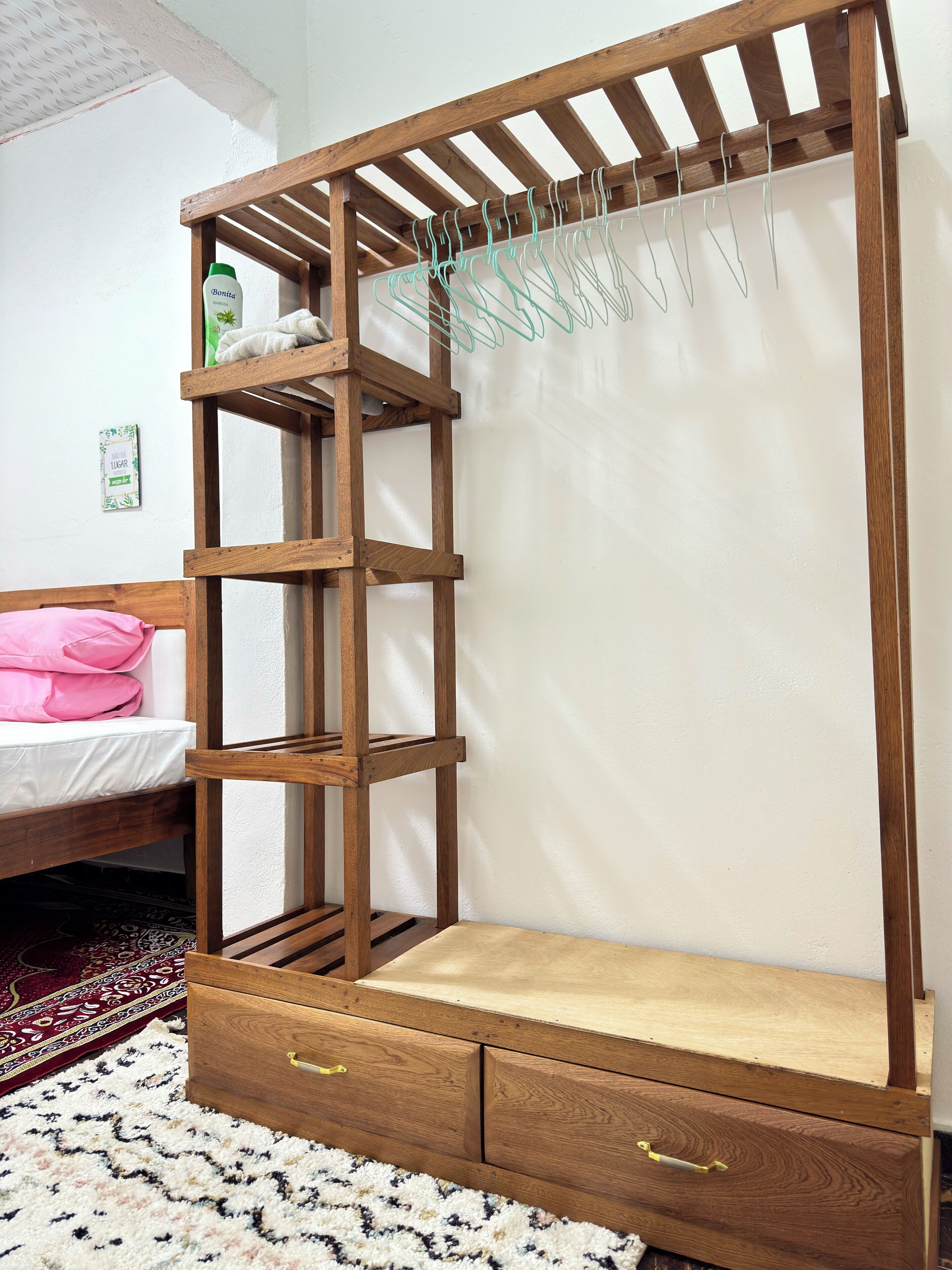 A wooden bunk bed with a built-in shelf and drawers, a hanging clothes rack, and a bedside table.
