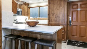 A kitchen with wooden cabinets, a large island with stools, a wooden bowl sink, and pendant lights. - Centrally Located 3 BR in Lionshead Village w/ Pool, Walk to Lift! (Vail)