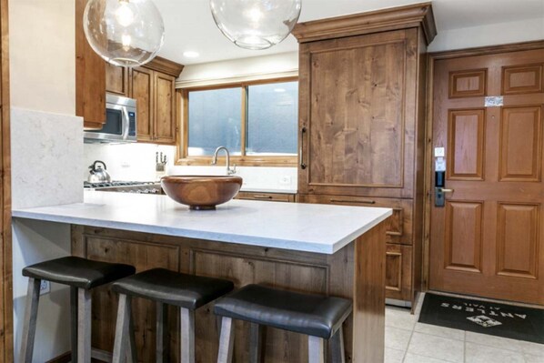 A kitchen with wooden cabinets, a large island with stools, a wooden bowl sink, and pendant lights.