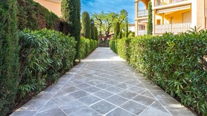 A pathway flanked by neatly trimmed hedges and a building with a balcony. - Le Clos Sainte Anne by Interhome (Saint-Tropez)