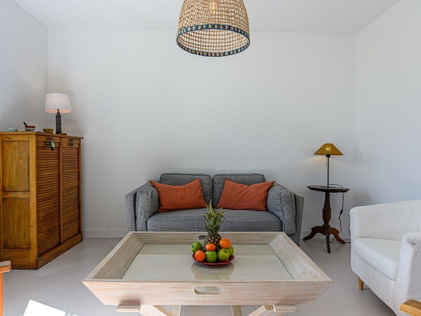 A living room with a grey sofa, a wooden cabinet, a coffee table with fruit, and a hanging light fixture.