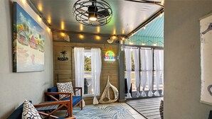Ein raum im Strandhausstil mit Wandgemälde, Holzmöbeln, einer Segelboot-Dekoration und Blick auf den Strand durch große Fenster.