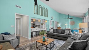 Ein Wohnzimmer mit grauem Sofa, einem Couchtisch und einem Essbereich, mit einer Küche im Hintergrund.