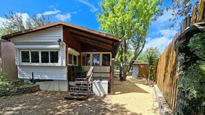 Une petite cabane avec une véranda, une allée en gravier et une clôture en bois.
