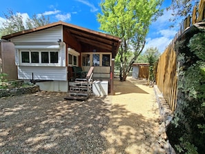 A small cabin with a porch, a gravel driveway, and a wooden fence.