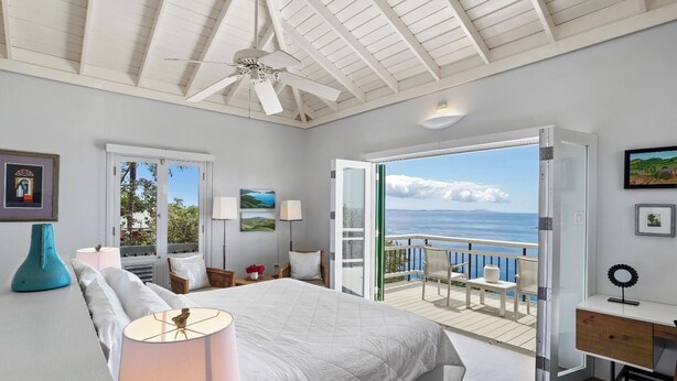 Ein Schlafzimmer mit einem großen Bett, einem Deckenventilator und einem Balkon mit Meerblick.