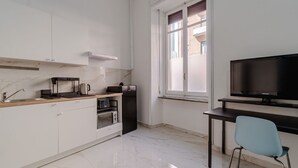 A compact kitchen with a microwave, toaster, and coffee maker, a black refrigerator, a dining table with a chair, and a TV. - GuestHost - Comfortable Studio Apartment GIOVE- Torino (Torino)