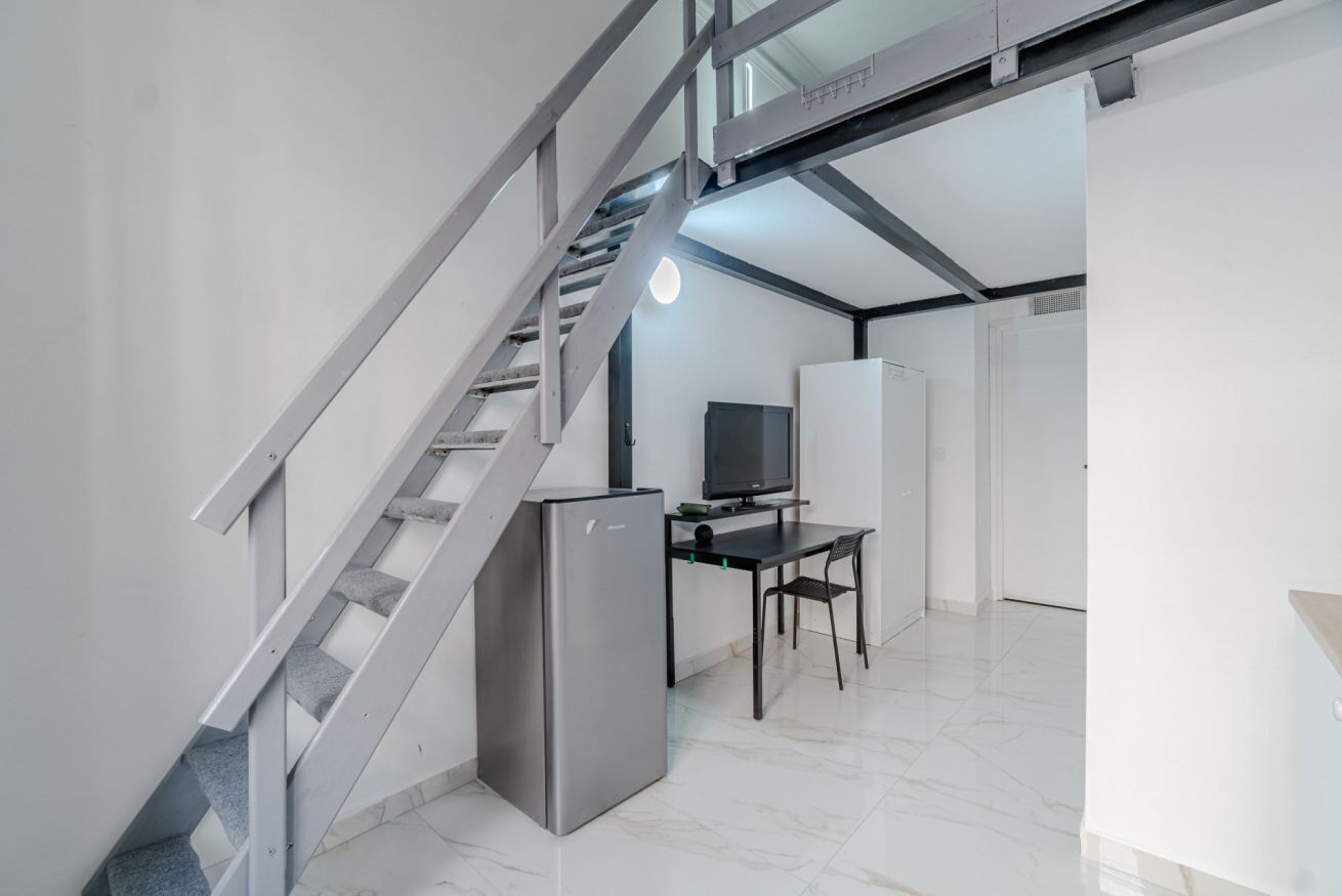 A modern interior with a staircase, a flat-screen TV, a refrigerator, and a dining area.