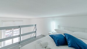 Ein Hotelzimmer mit Bett, Nachttisch, Fenster mit Blick auf parkende Autos und einem Balkongeländer.