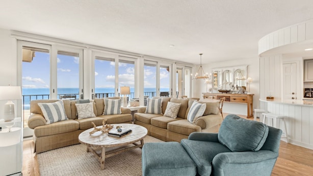 A spacious living room with a large sectional sofa, a round coffee table, and a view of the ocean through large windows.