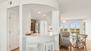 A modern kitchen with white cabinetry, a central island, and a dining area with a bench and chairs.