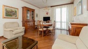A living room with a sofa, a glass coffee table, wooden cabinets, a dining table with chairs, a TV, and a chandelier. - GuestHost - Wonderful apartment of about 80 square meters, able to accommodate 5 people, located on the first floor of a villa without a lift (with internal and external steps).The property is located in the heart of Venice Mestre, in a quiet and well-se (Venice)