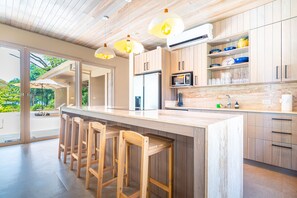 Une cuisine moderne avec des meubles en bois, un grand îlot central doté de tabourets et un éclairage suspendu.