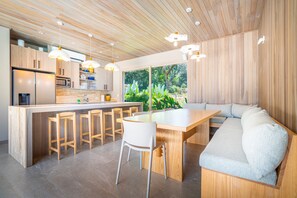 A modern kitchen with wooden cabinets, a central island with stools, and pendant lighting.