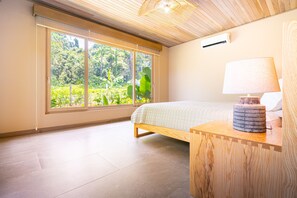 Une chambre avec une grande fenêtre, un lit, une table de chevet avec une lampe et un plafond en bois.