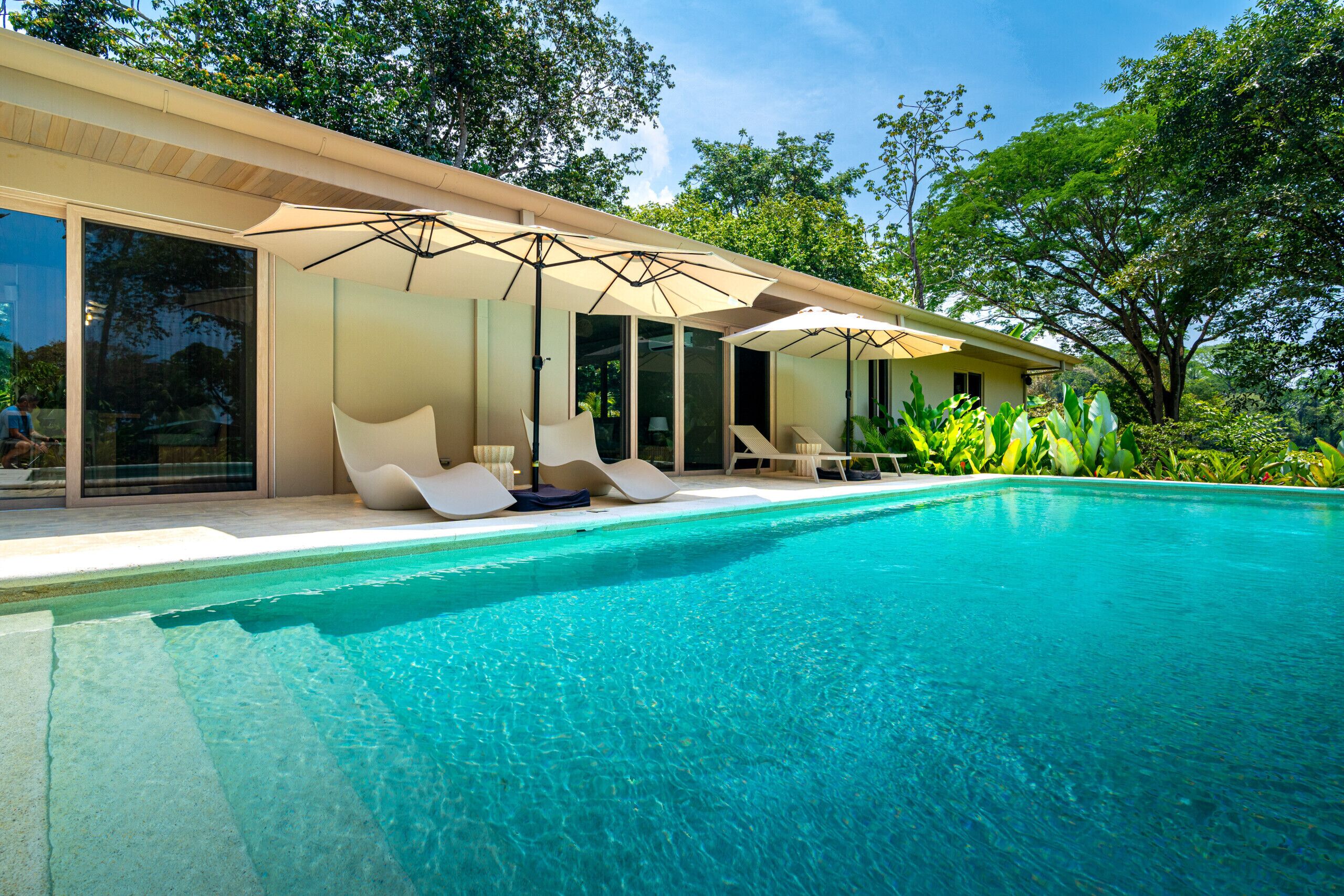 A modern poolside area with a clear blue pool, sun loungers, and umbrellas.