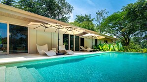 A modern poolside area with a clear blue pool, sun loungers, and umbrellas.