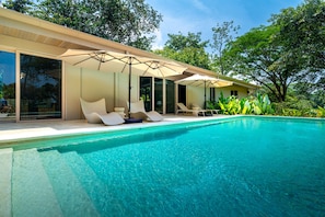 A modern poolside area with a clear blue pool, sun loungers, and umbrellas.