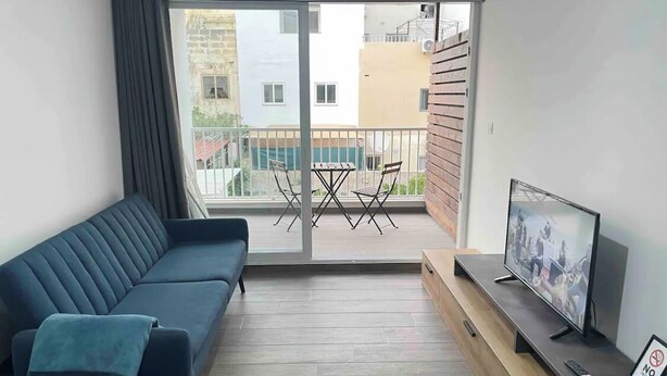 Una sala de estar moderna con un sofá, un televisor y un balcón con mesa y sillas.