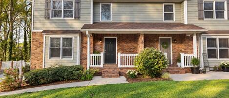 A two-story residential building with a brick facade, white trim, and a front porch with a black door.