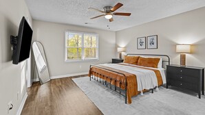 A bedroom with a bed, bedside tables, a ceiling fan, a TV, and a window.