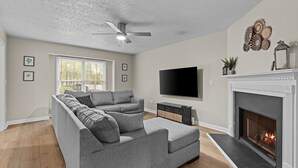 A living room with a sectional sofa, a fireplace, a flat-screen TV, and a ceiling fan.