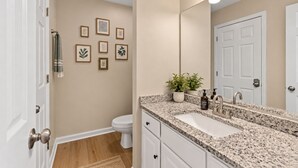 Un baño con encimera de granito, un lavabo blanco, un espejo e impresiones botánicas enmarcadas en la pared.