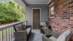 A porch with wicker furniture, a door, and a brick wall.