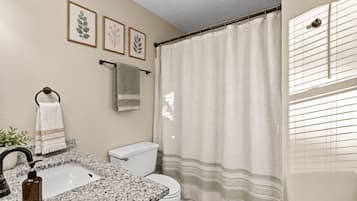 A bathroom with a granite countertop sink, a toilet, and a shower curtain.