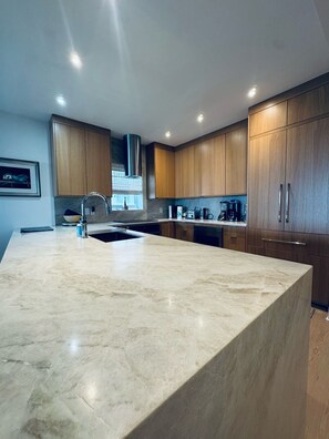 Una cocina moderna con una isla grande de mármol, armarios de madera y electrodomésticos integrados.