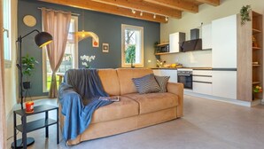 A cozy living room with a sofa, a lamp, and a kitchen area with cabinets and appliances. - GuestHost - Oasis of the Knight! (Ferrara)