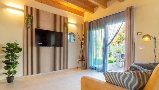 A modern living room with a flat-screen TV, a sofa, a potted plant, and a large window with curtains. - GuestHost - Oasis of the Knight! (Ferrara)
