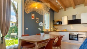 A modern kitchen with white cabinets, a built-in oven, and a dining area with a wooden table and red chairs. - GuestHost - Oasis of the Knight! (Ferrara)